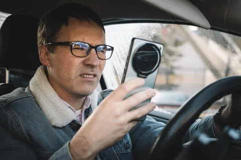 Distracted driver checking a smartphone while driving, viewing messages or .. Stock Photos
