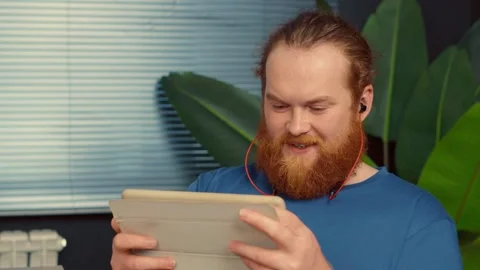 Distracted man with red beard playing games on tablet at work Stock Footage 340813473