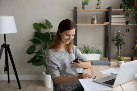 Distracted from online computer work young woman using smartphone. Stock Photos