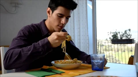 Distracted young man sitting enjoying his meal of spaghetti, then drinking water Stock Footage 50075890