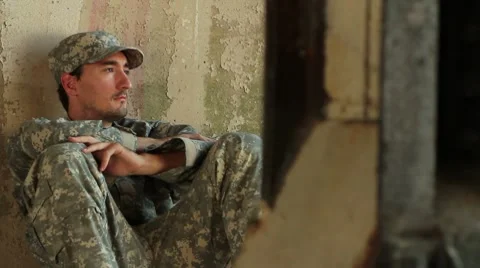 Distraught soldier sitting against concrete wall Stock Footage