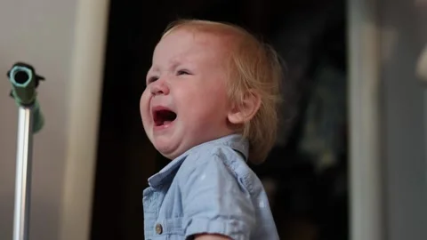 A distressed toddler crying while standing in a room with a metal pole in the Stock Footage 345610971