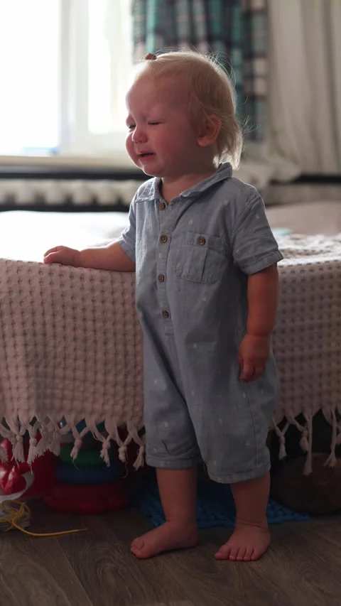 A distressed toddler crying while standing and holding onto the edge of a bed in Stock Footage 345611000