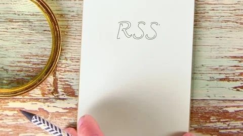 On a distressed wood table, a hand writes the letters RSS on a notepad. A golden Stock Footage 327013115