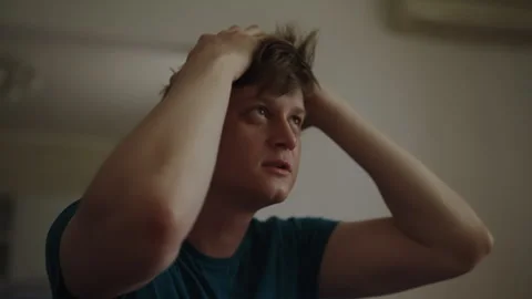 Distressed young man sitting at home, clutching head in despair and feeling Stock Footage 342813123