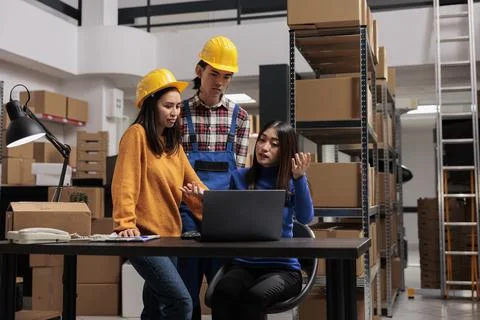 Distribution center workers checking goods supply schedule on laptop Foto stock