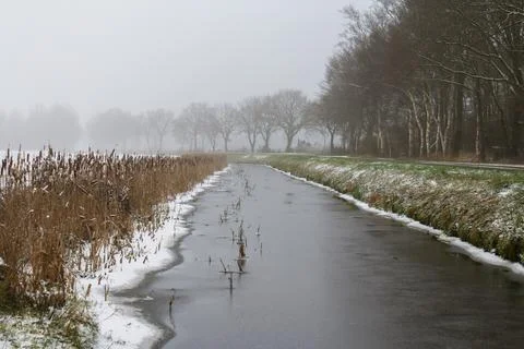 Ditch along the road with a thin layer of ice, snow on the sides of the ditc Stock Photos
