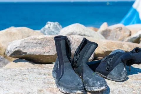 Dive boots drying on a stone. A dive flag and blue water in the background Stock Photos