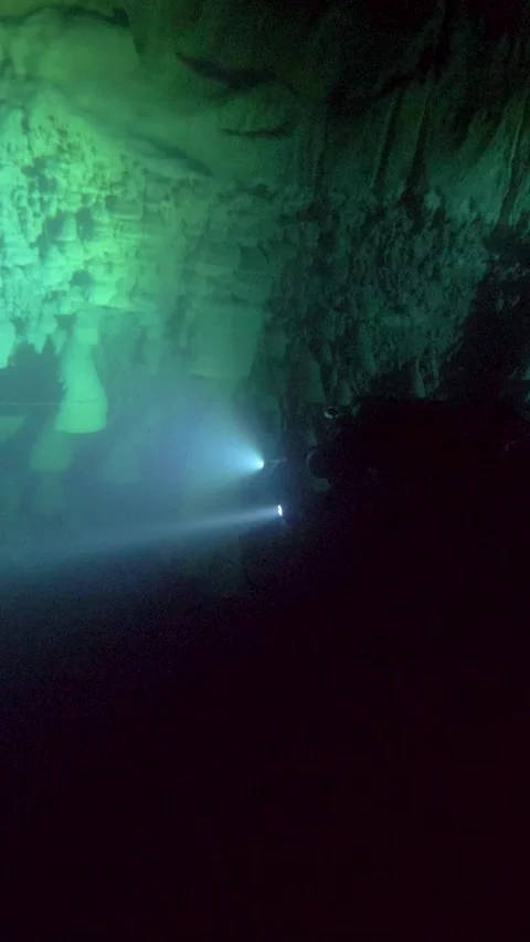 Dive light scans a rough rocky wall inside a dark cenote Stock Footage 341396123