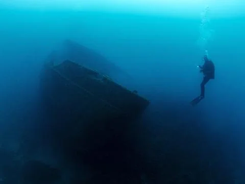 Diver diving in front of the remains of a sunken ship Stock Photos