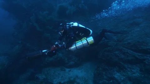 Diver with DPV runs alongside rocks on the seabed, Ustica, Mediterranean sea Stock Footage 127386481