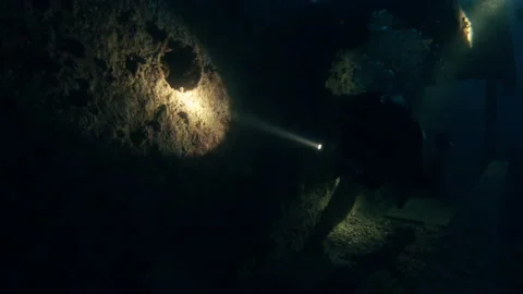 Diver exploring sunken vessel underwater, shining with flashlight in darkness Stock Footage 223354921