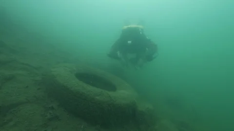 Diver with frying pan and net swims over a tire, Albano lake, Italy Stock Footage 107566447