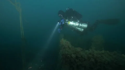 Diver lights up the wreck Adernò from bow to block with pulley bearing ropes  Stock Footage 228215783