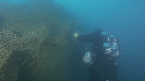 Diver with torch explores swimming part of the wreck Aderno' wrapped in a net Stock Footage 227432952