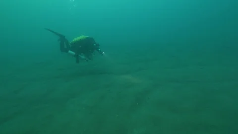 Diver with torch swims at the bottom of the lake, San Domenico lake, Italy Stock Footage 108679476