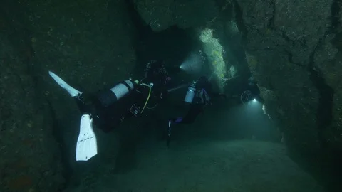 Divers illuminate the sandy bottom in the crack between rocks, Ustica, Med sea Stock Footage 126974592