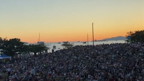 Diverse Anonymous crowd and spectators sitting on grass hill during sunset Stock Footage 281916425