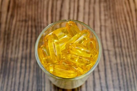 Diverse array of yellow gel capsules in a glass on a wooden surface 写真素材
