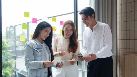 Diverse Asian creative team brainstorming with sticky notes and smartphone in Stock Photos
