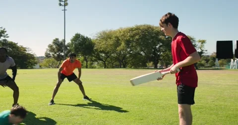 Diverse athletes training cricket at park, batsman bouncing red ball, swinging Stock Footage 340964103