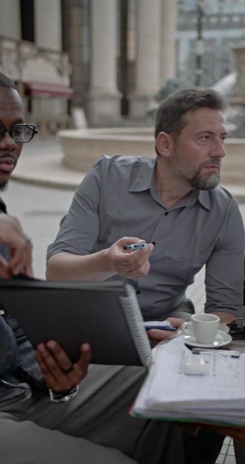 Diverse Business Professionals Discussing Work and Ideas in an Outdoor Cafe Stock Footage 315820558