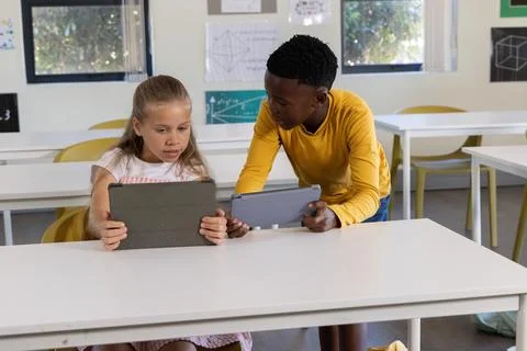 Diverse children collaborating on tablets at front classroom with patterned Stock Photos