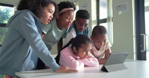 Diverse children crowding at school table with tablet, reacting to content by Stock Footage 341736397