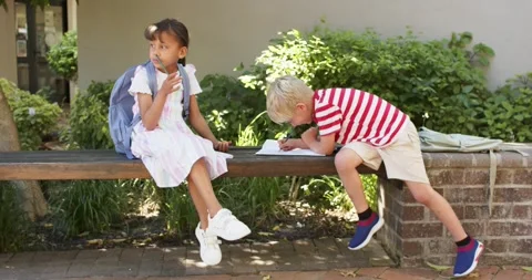 Diverse children sitting on bench at school seeing open notebook doing homework Stock Footage 342927909