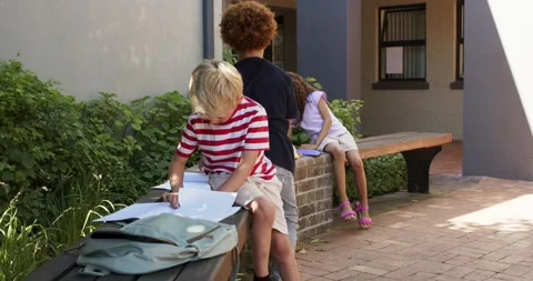 Diverse children sitting courtyard, backpack urging blond boy spreading papers Stock Footage 340069717