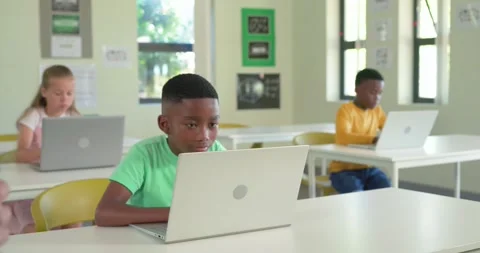 Diverse children typing on silver laptops at desks, front student in green T 库存影片 335625206