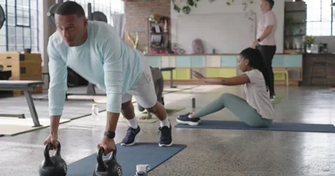 Diverse class starting circuit at loft gym, man doing kettlebell plank rows on Stock Footage 338356648
