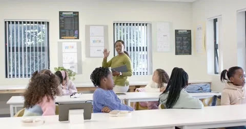 Diverse class teacher raising hand with tablet, calling, elementary kids turning Stock Footage 341028436