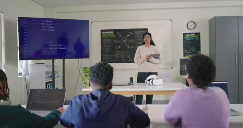 Diverse class teacher using tablet teaching code while monitor showing, teens Stock Footage 340811433