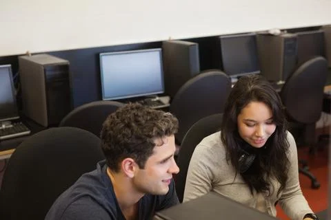 Diverse classmates collaborating on PCs in computer lab, headphones and Stock-Fotos