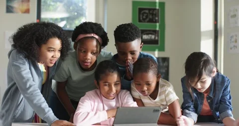 Diverse classmates leaning around tablet on low table at school, watching Stock Footage 336897494