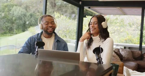 Diverse co-hosts laughing after joke and gesturing to mic while checking notes Stock Footage 341937256