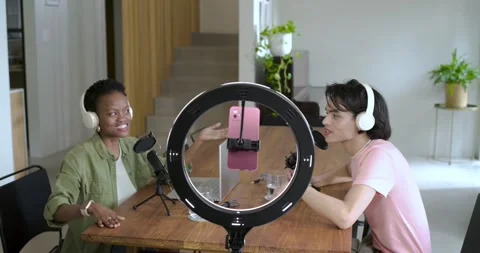 Diverse co-hosts leaning into mics discussing and gesturing at wooden table Stock Footage 336897411