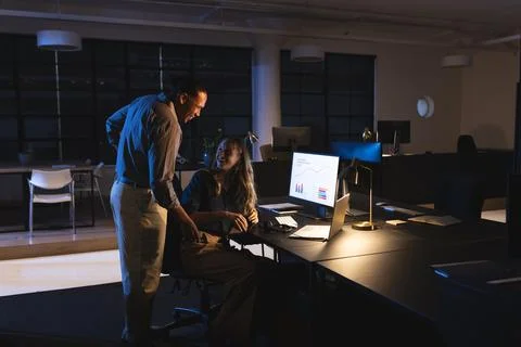 Diverse colleagues collaborating on project in dimly lit office, discussing data Stock Photos