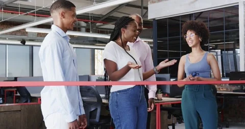 Diverse colleagues cutting ribbon in modern office interior, using laptops and Stock Footage 316945672
