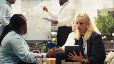 Diverse colleagues discuss planning notes beside laptop at outdoor meeting Stock Footage 338383133