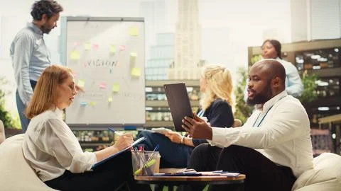 Diverse colleagues discuss planning notes beside laptop at outdoor discussion Stock Photos
