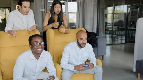 Diverse colleagues enjoy a lively console game break in a modern office, Stock Footage 335766570