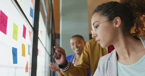 Diverse colleagues jot down ideas on memo notes, brainstorming on glass wall Vidéo 336657545