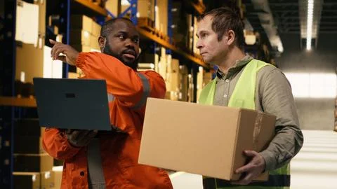 Diverse colleagues moving cargo in boxes using laptop for inventory control Stock Photos
