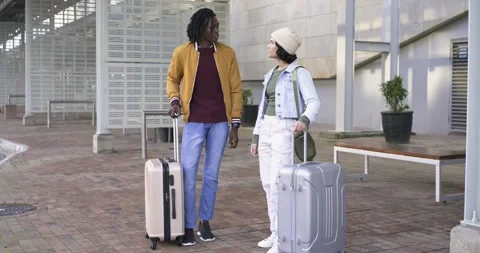 Diverse couple arriving at courtyard pulling suitcases, chatting then raising Stock Footage 341936989