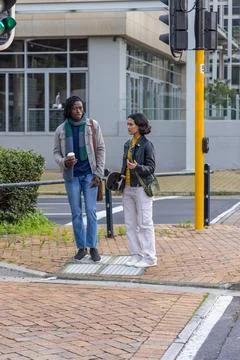 Diverse couple chatting while waiting at street crossing holding coffee cup, Fotos Stock