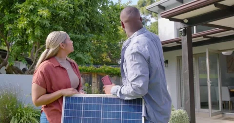 Diverse couple checking install info on phone in yard, holding solar panel and Stock Footage 340969847