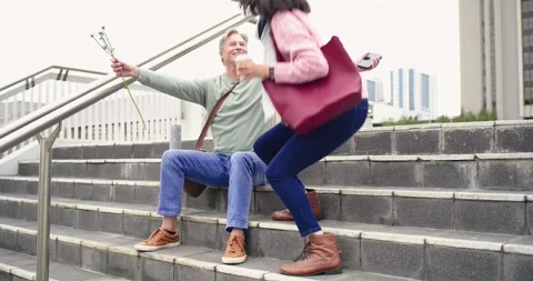 Diverse couple checking smartphone and hugging at partner arrival on steps with Stock Footage 341089445