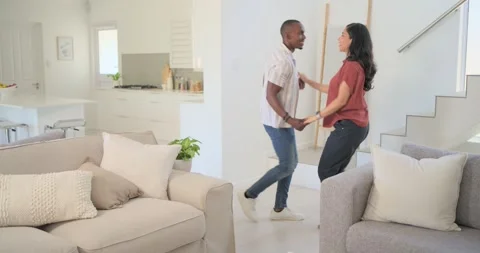 Diverse couple clasping hands and dancing playfully by coffee table near Stock Footage 336175103